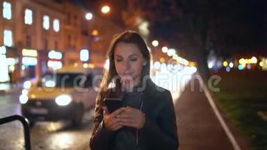 迷人的女人在夜城的<strong>街道</strong>上<strong>行走</strong>时使用智能手机